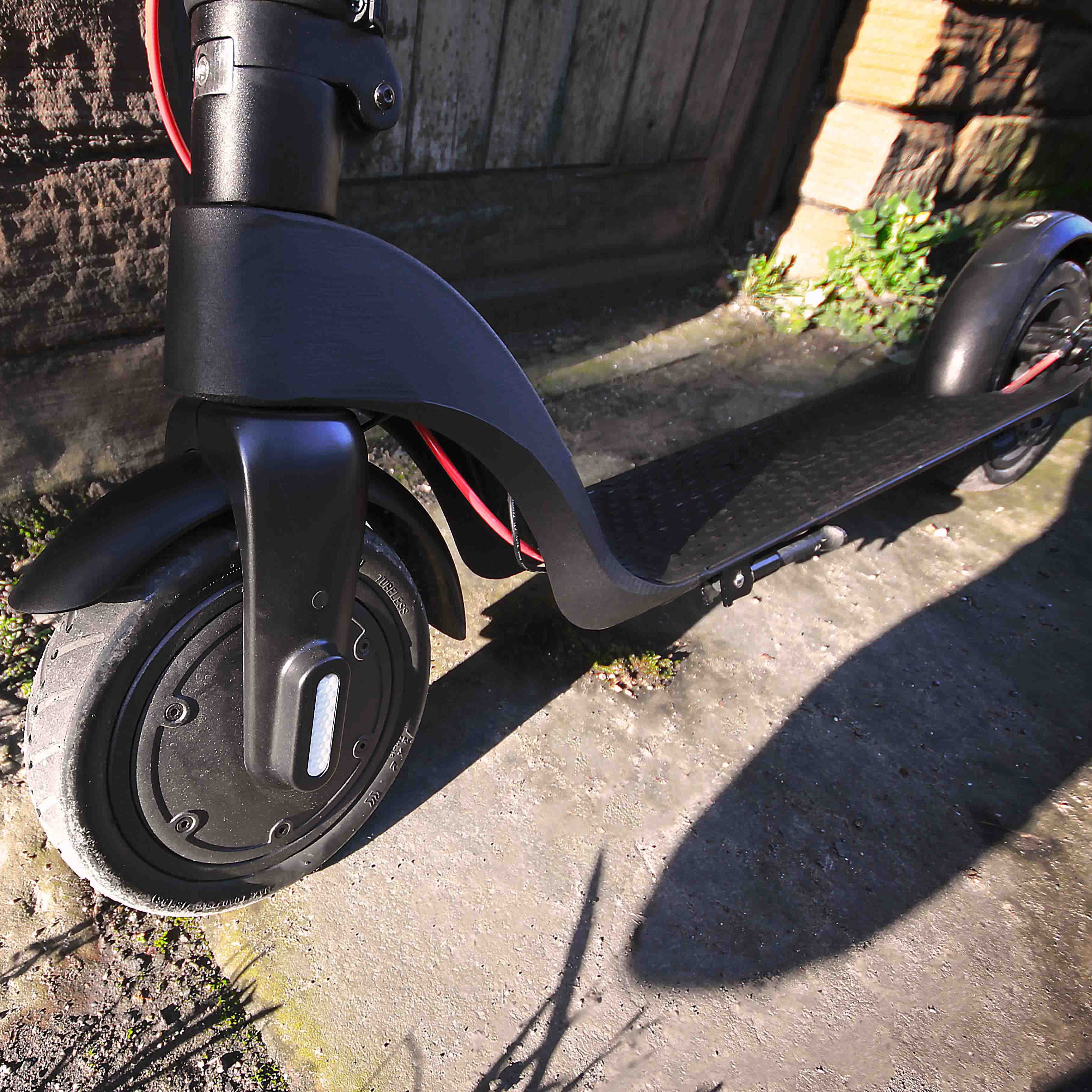 Black electric scooter on a stone pavement with a stone wall in the background.