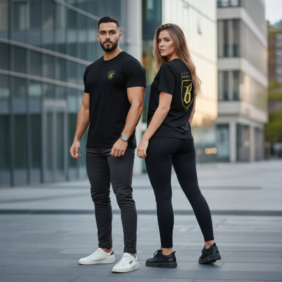 Man and woman wearing matching black barugzai gold and black t-shirts with logos in an urban setting.