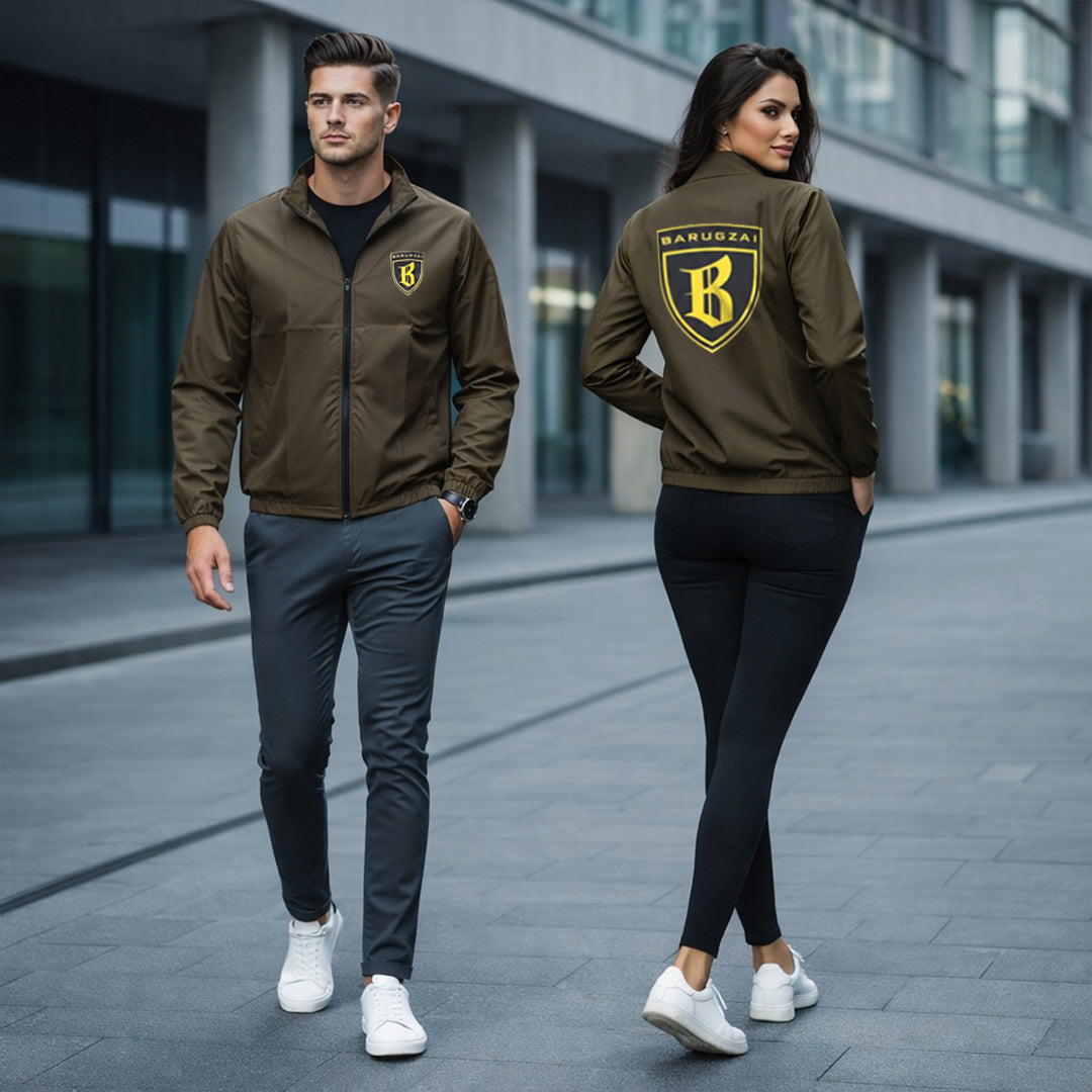 Two people wearing matching olive brown jackets with a logo on a city street.