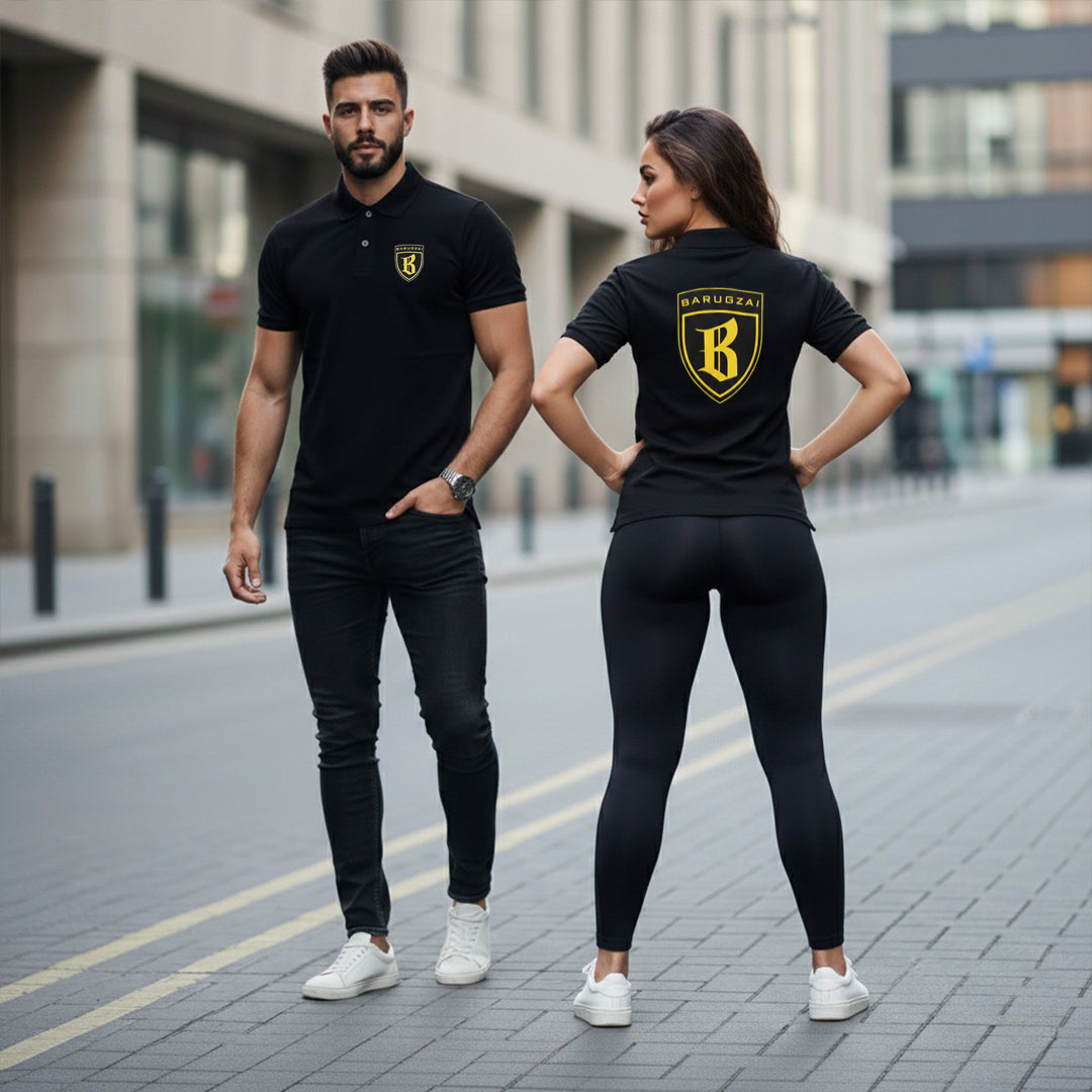 Man and woman wearing matching black outfits with a gold & black logos on a city street.