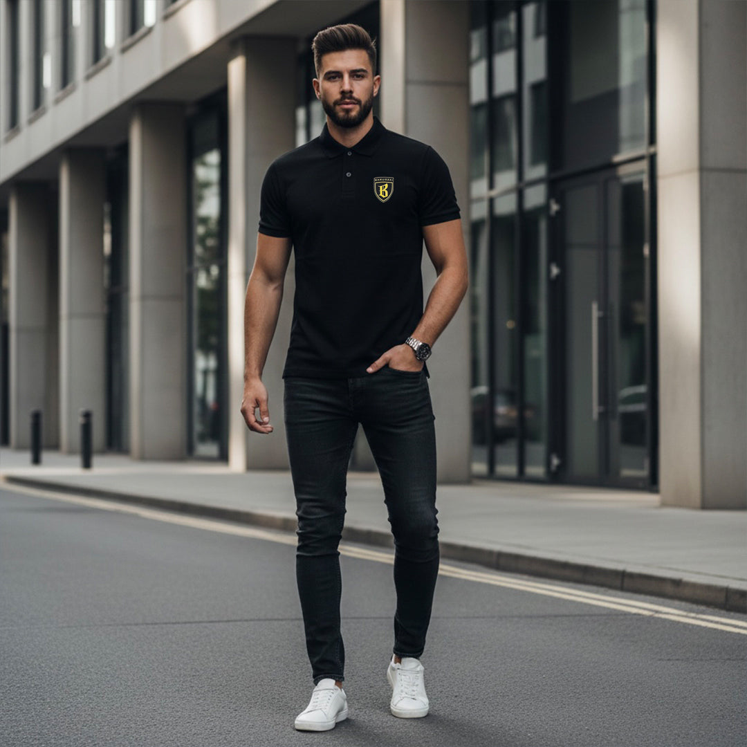 Man wearing a black polo shirt with a logo and dark jeans standing on a city street.