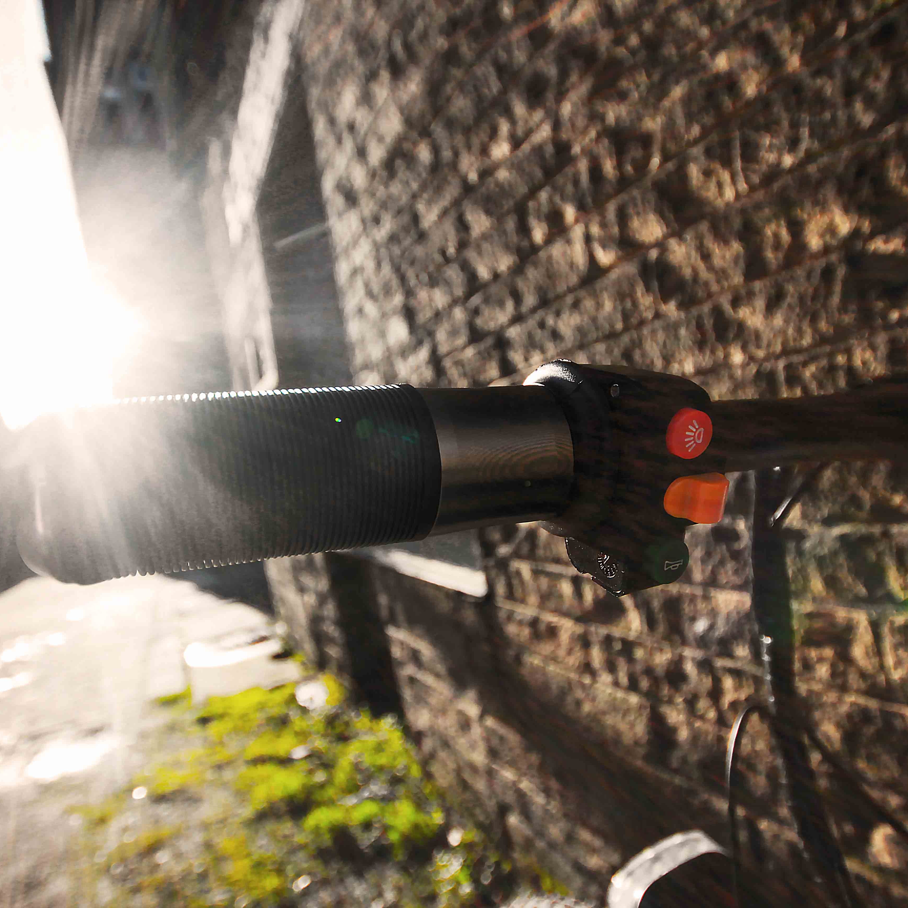 Close-up of a bicycle handlebar with a light shining on it, against a blurred natural background.