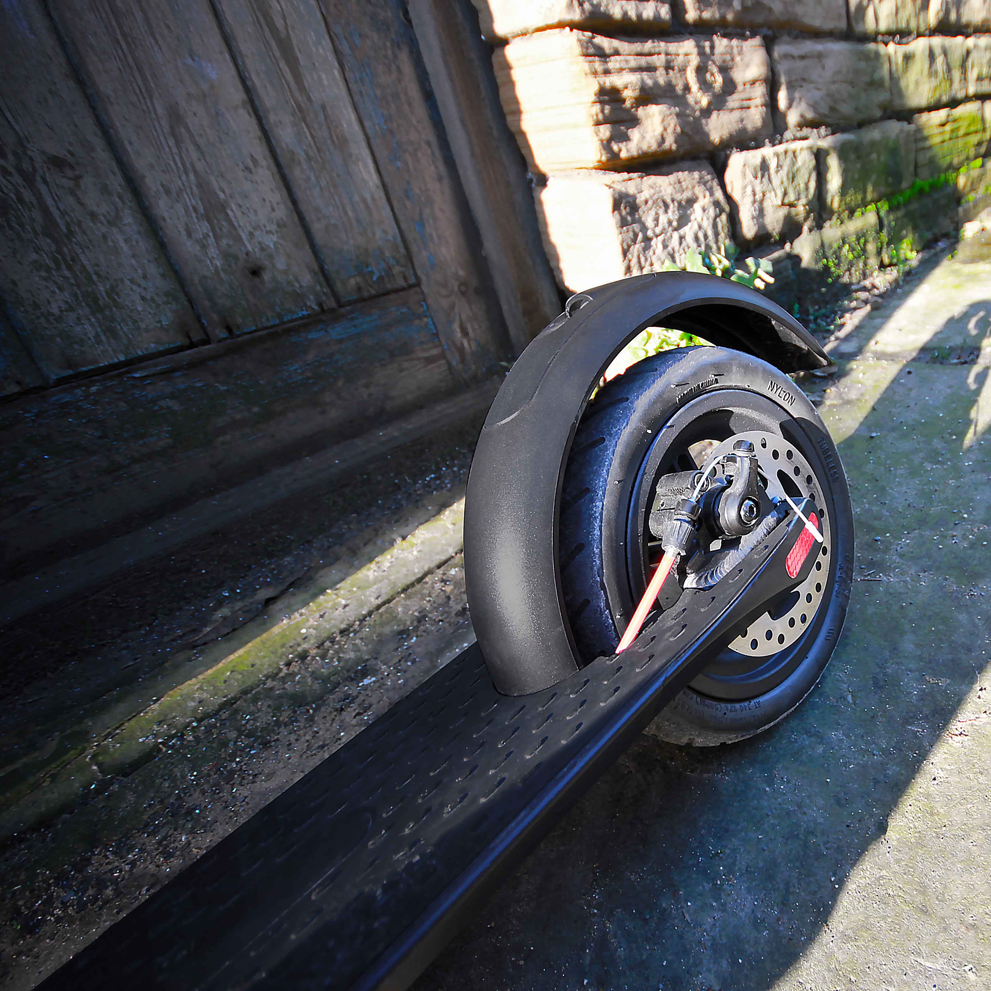 Wheel of a scooter on a stone surface with a wooden bench and stone wall in the background.