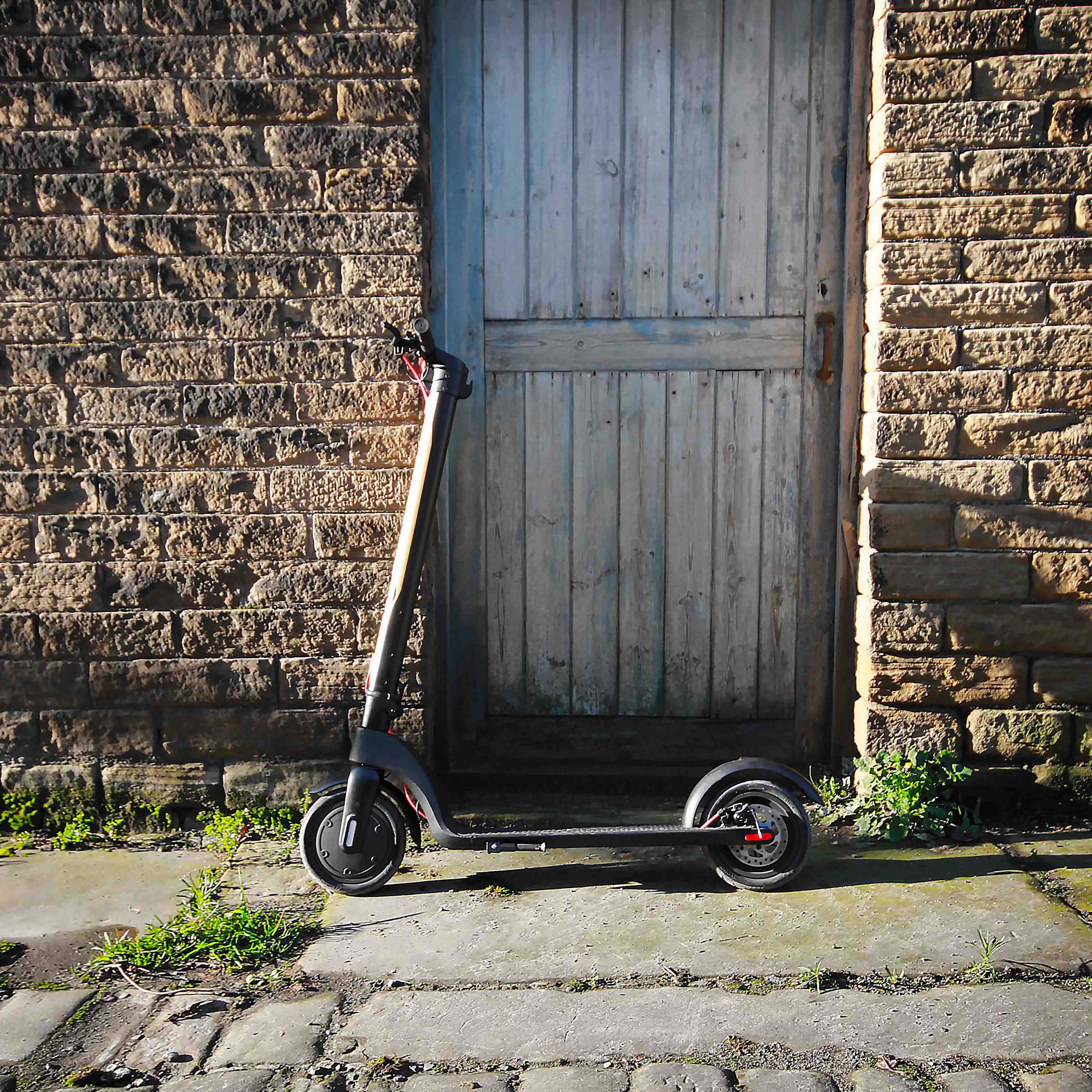 Electric scooter leaning against a brick wall with a wooden door.