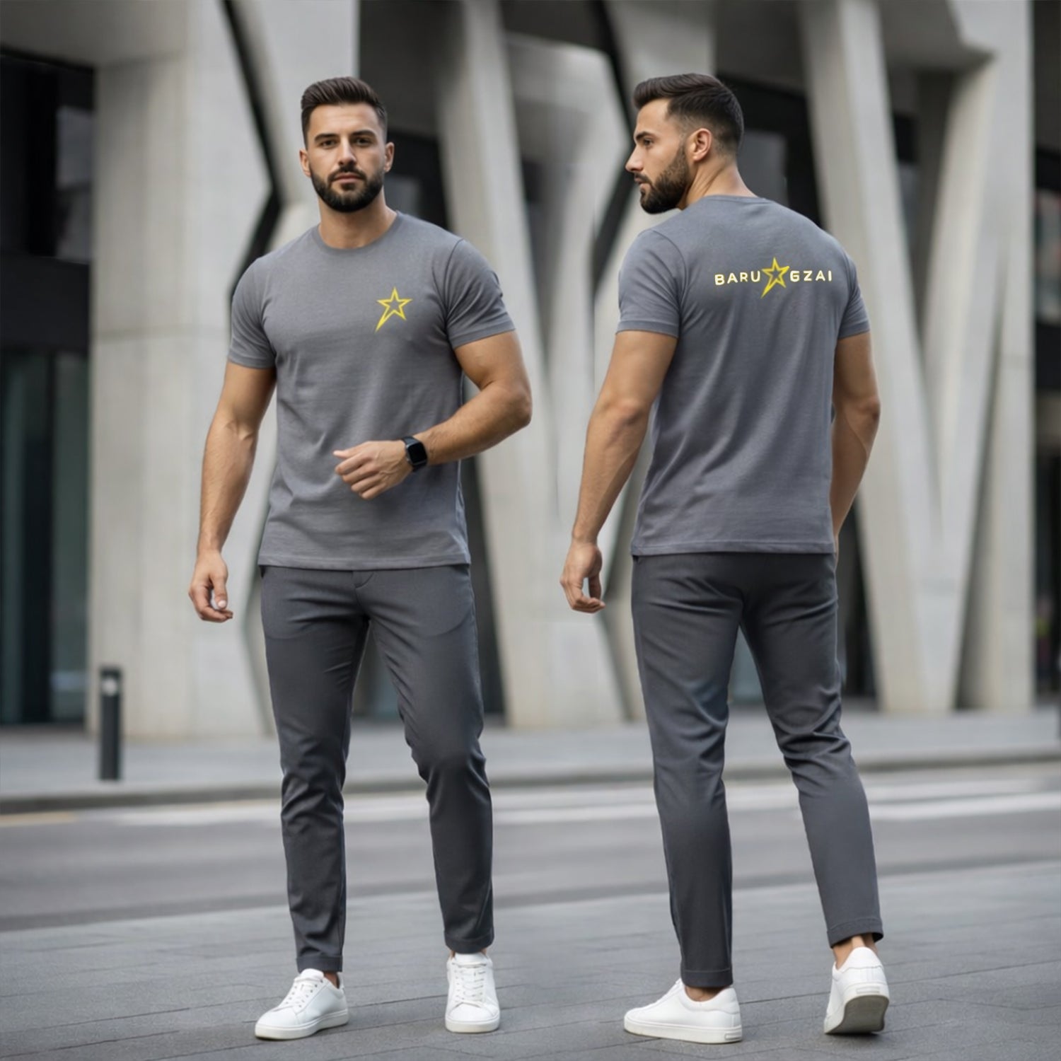 Man wearing a gray t-shirt with a logo and dark pants, standing in front of a modern building.