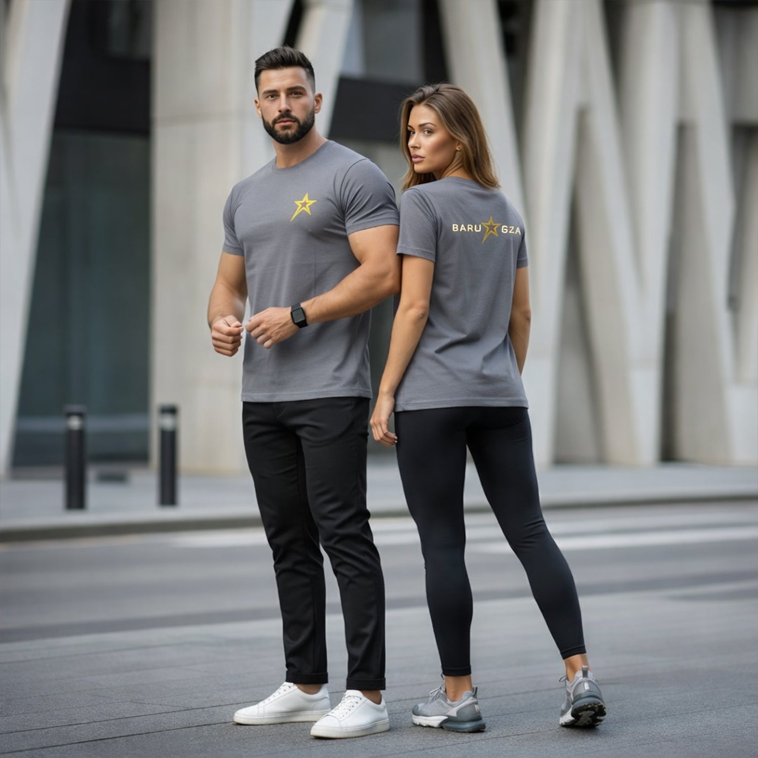 Man and woman wearing matching gray t-shirts with a logo, standing on a city street.