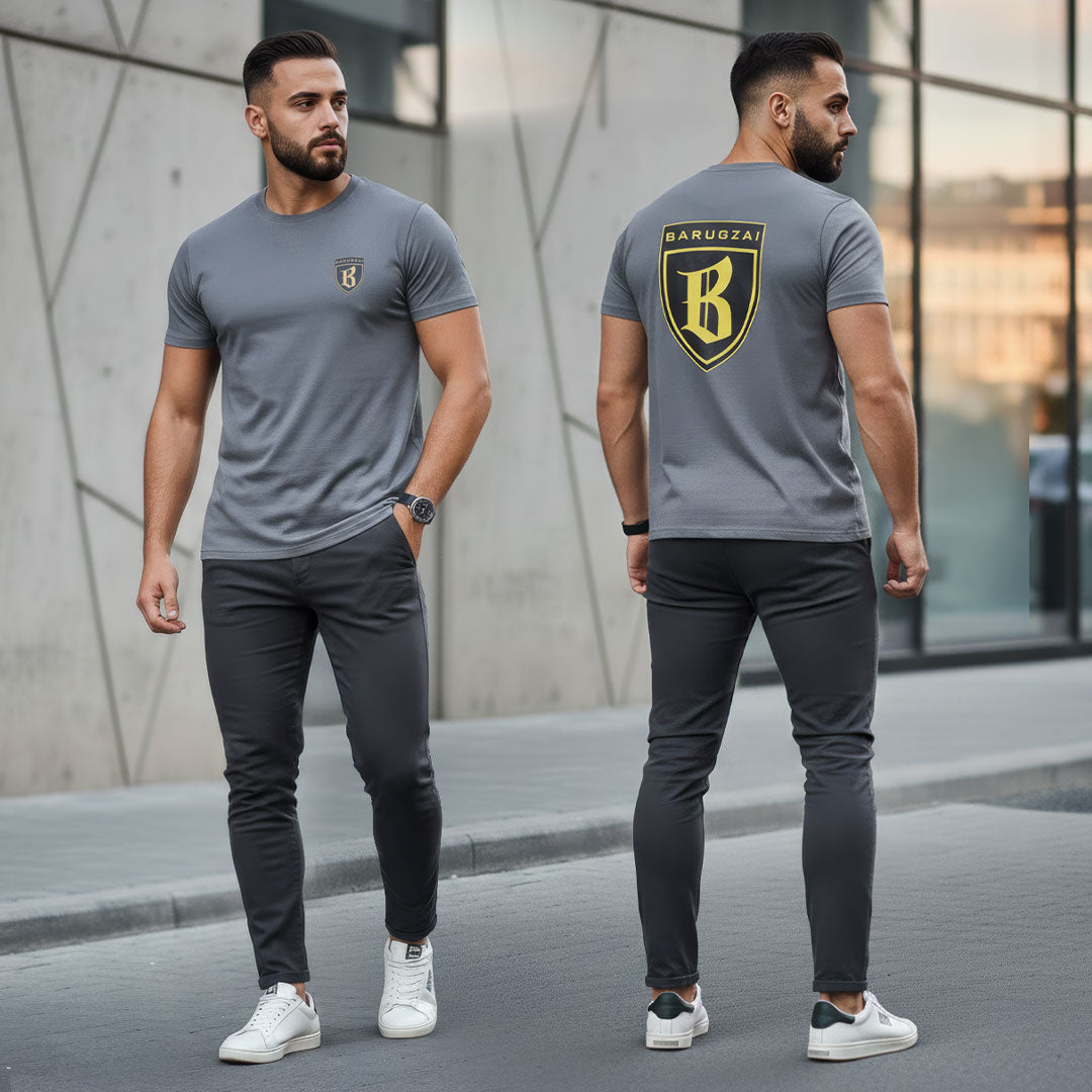 Man wearing a gray t-shirt with a barugzai gold and black logo on the front and back, standing in an urban setting.